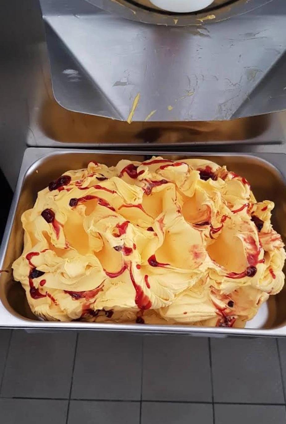 Frisch hergestelltes Eis in der Edelstahlwanne, cremig gelb mit Fruchtsoße durchzogen