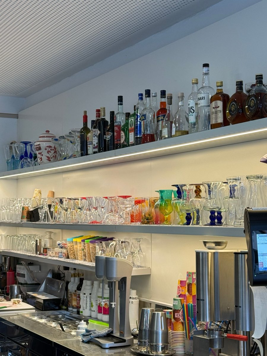 Regal mit bunten Eisbechergläsern und Likörflaschen hinter der Theke