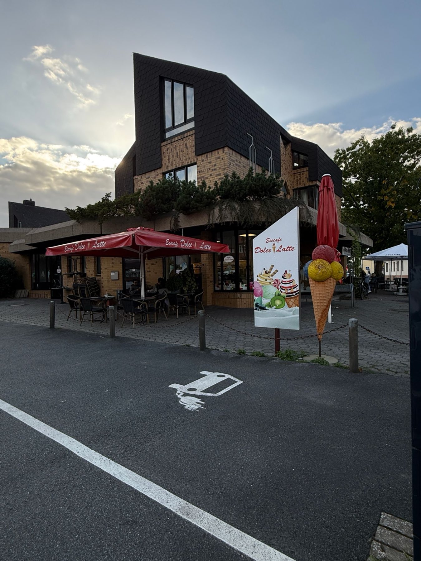 Das Eiscafé Dolce Latte in Bissendorf am Abend, mit roten Sonnenschirmen und der großen Eistüte vor dem Eingang