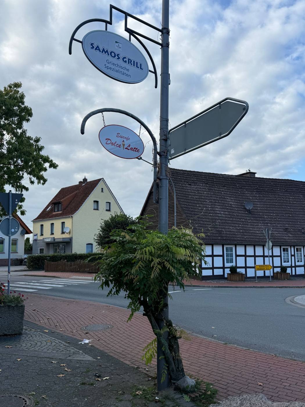 Hängeschild des Eiscafés Dolce Latte an der Straßenkreuzung in Bissendorf, dahinter ein Fachwerkhaus