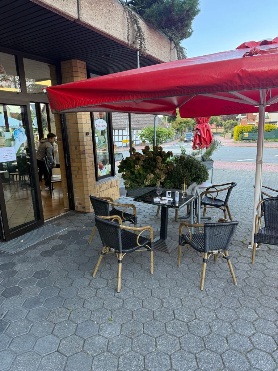 Terrasse des Eiscafés mit Tischen und Korbstühlen unter einem roten Sonnenschirm
